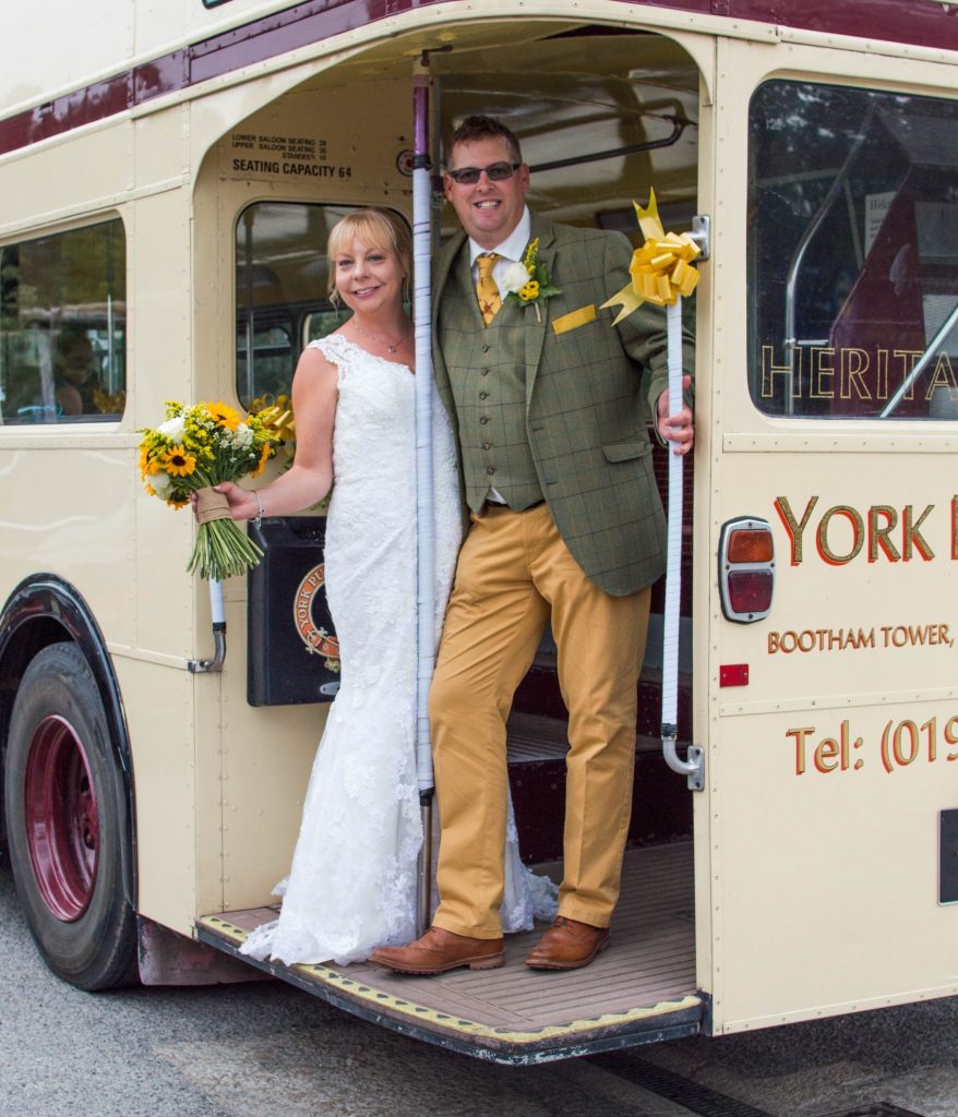 Bride and groom on york pullman wedding bus. Bride holds a wedding bouquet of mini sunflowers, roses, solidago and daisies.